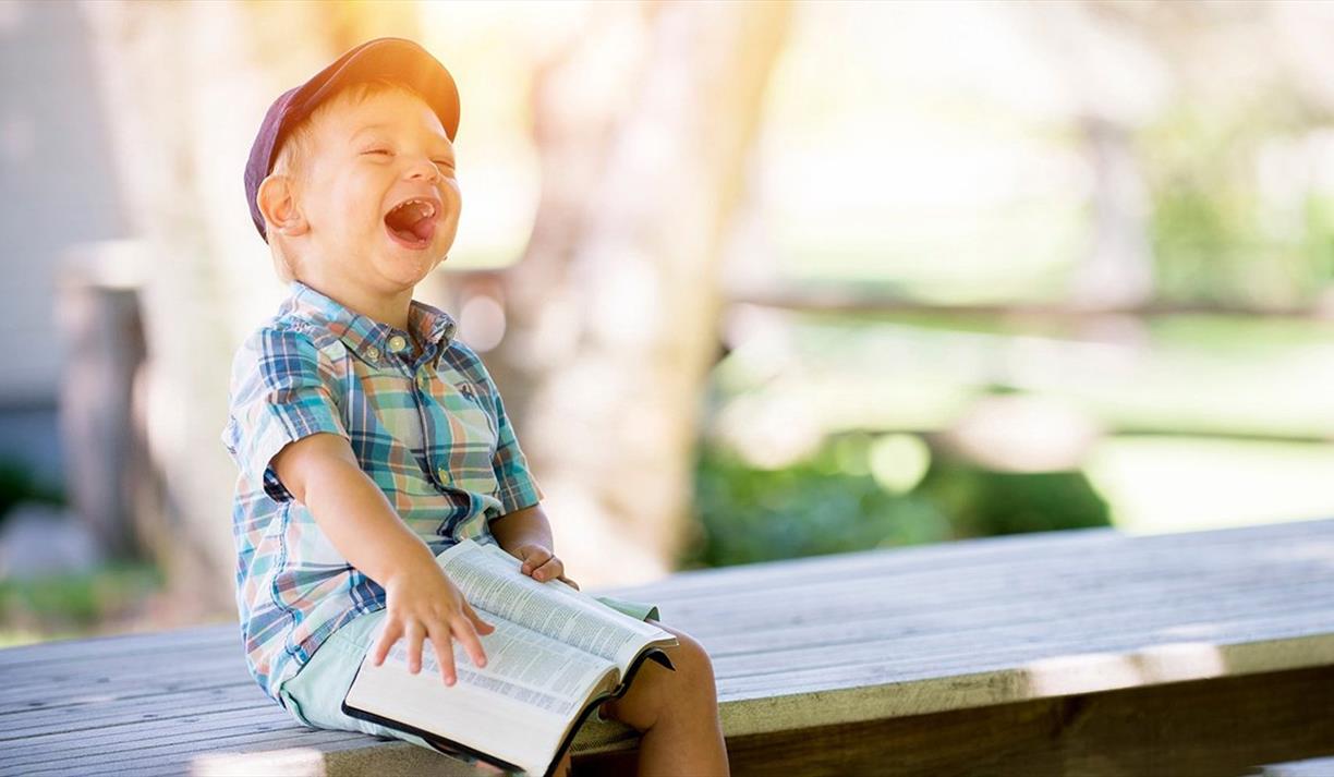 Boy sitting with book on a bench and laughing