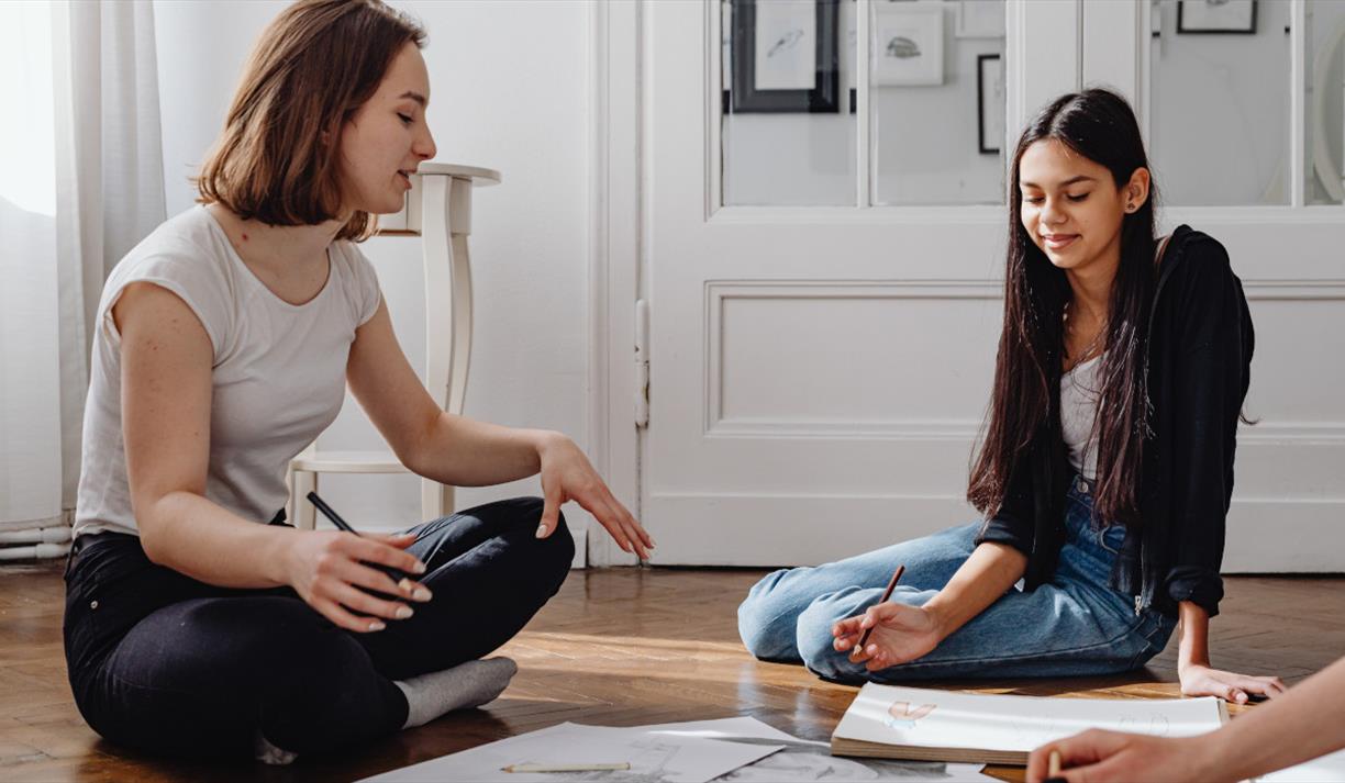 Two people sat on the floor between art supplies