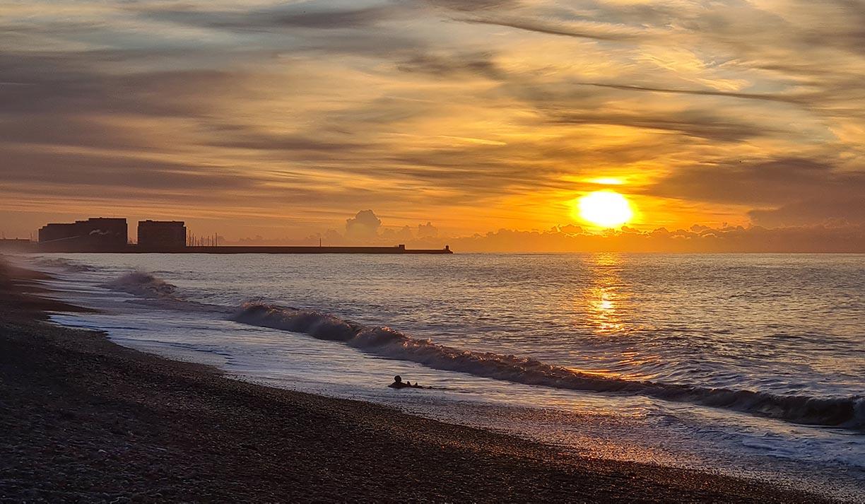 Photo of Brighton beach at sunrise. Brighton Marina is on the horizon.