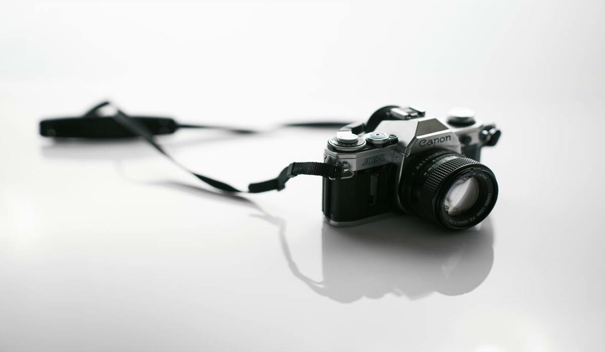 Classic vintage film camera with a lens and strap on reflective white background