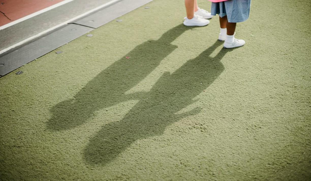 Two children casting shadows on a green surface