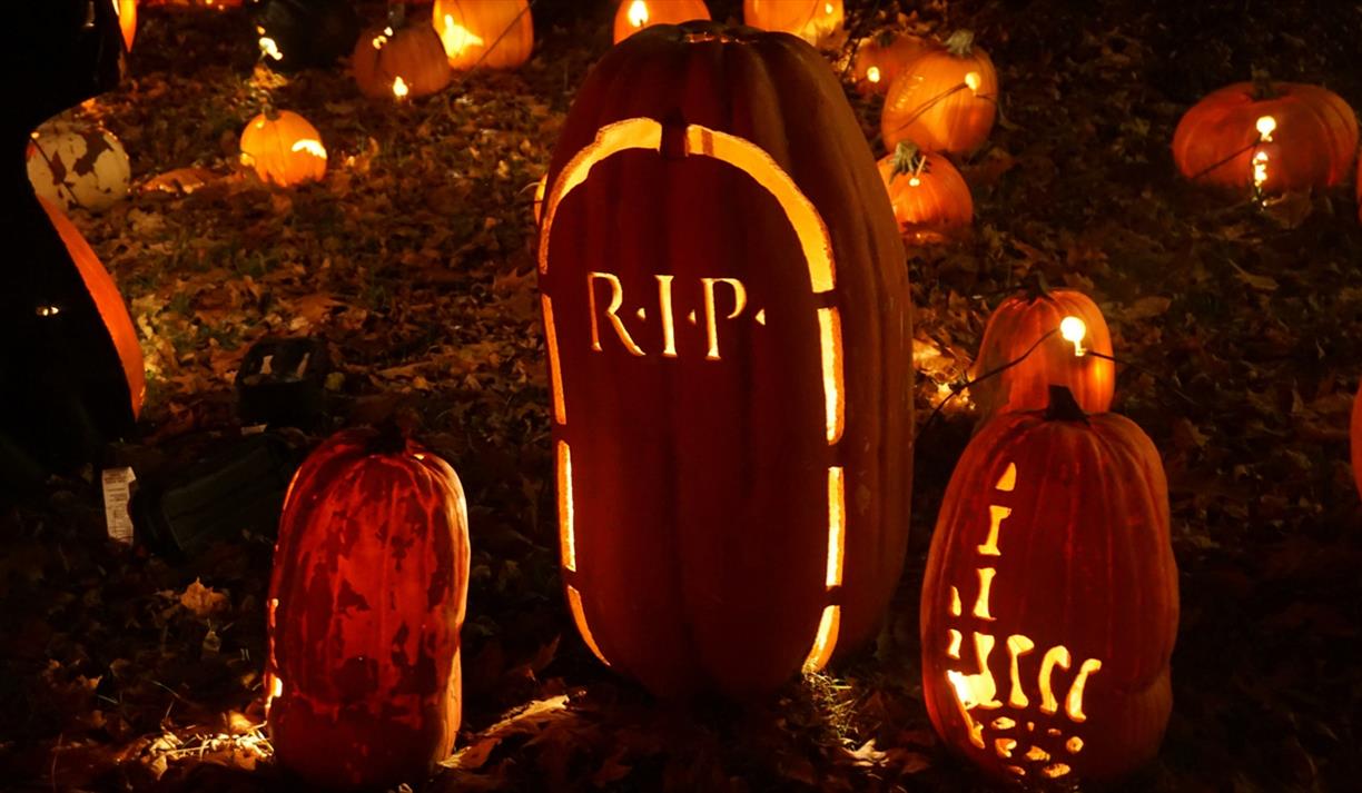 Two pumpkins carved with a skeleton hand pointing up and a tombstone
