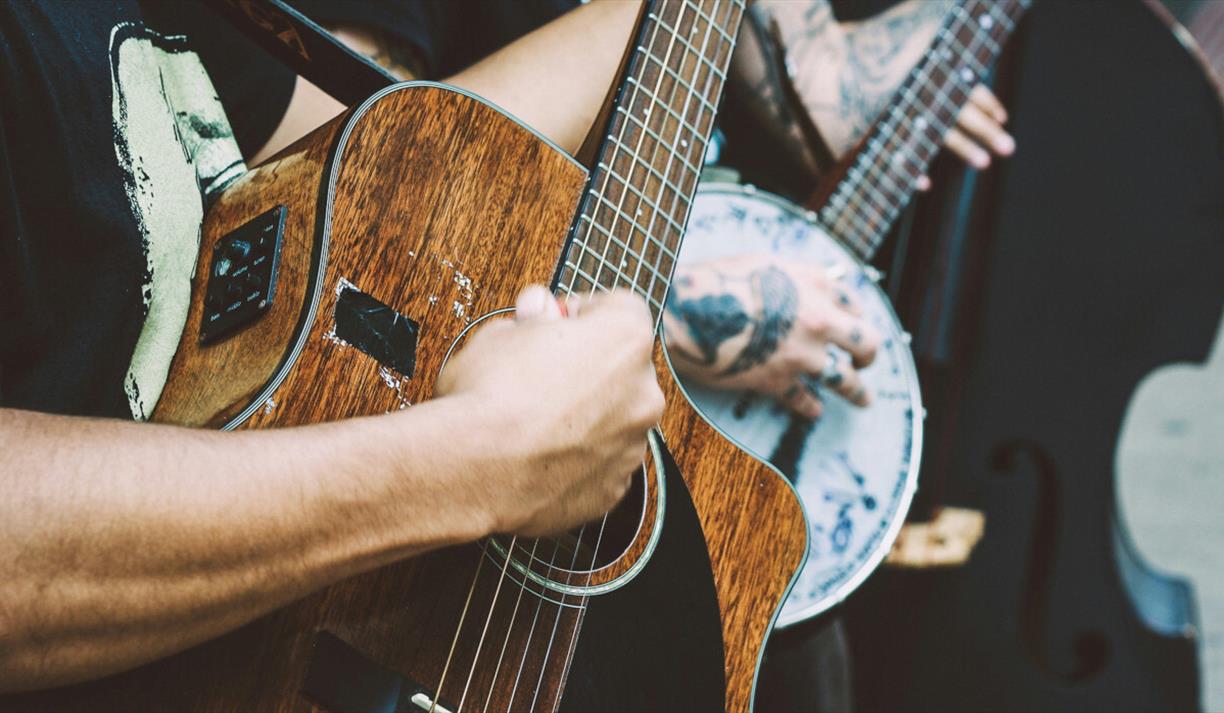 Person playing a banjo and another playing a dark wood acoustic guitar and another with a double bass