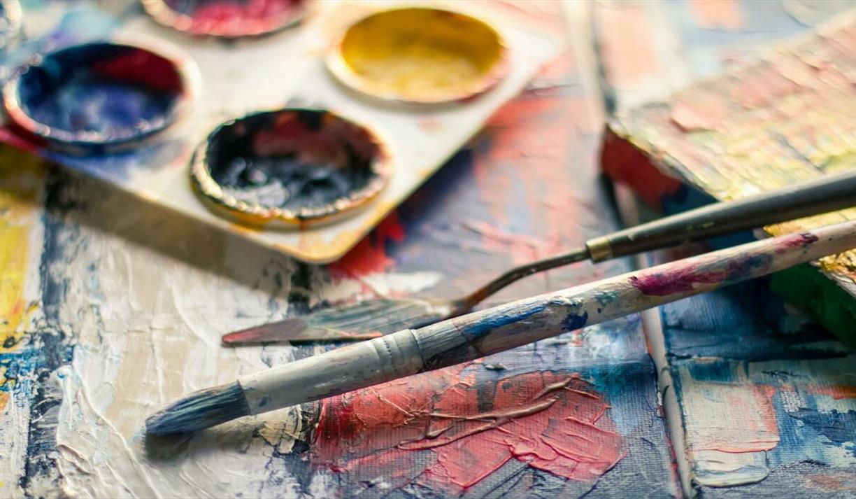 Close-up of colourful paintbrushes and artist palette on a textured canvas