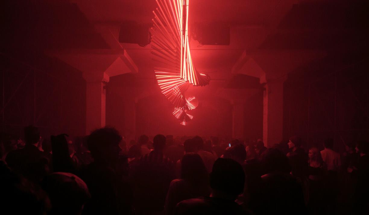 Twisting red neon strip lights in a dark room above a dancing crowd