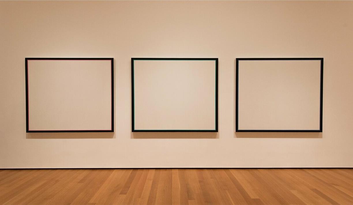 Three blank canvases on a white wall in a gallery with wooden floorboards
