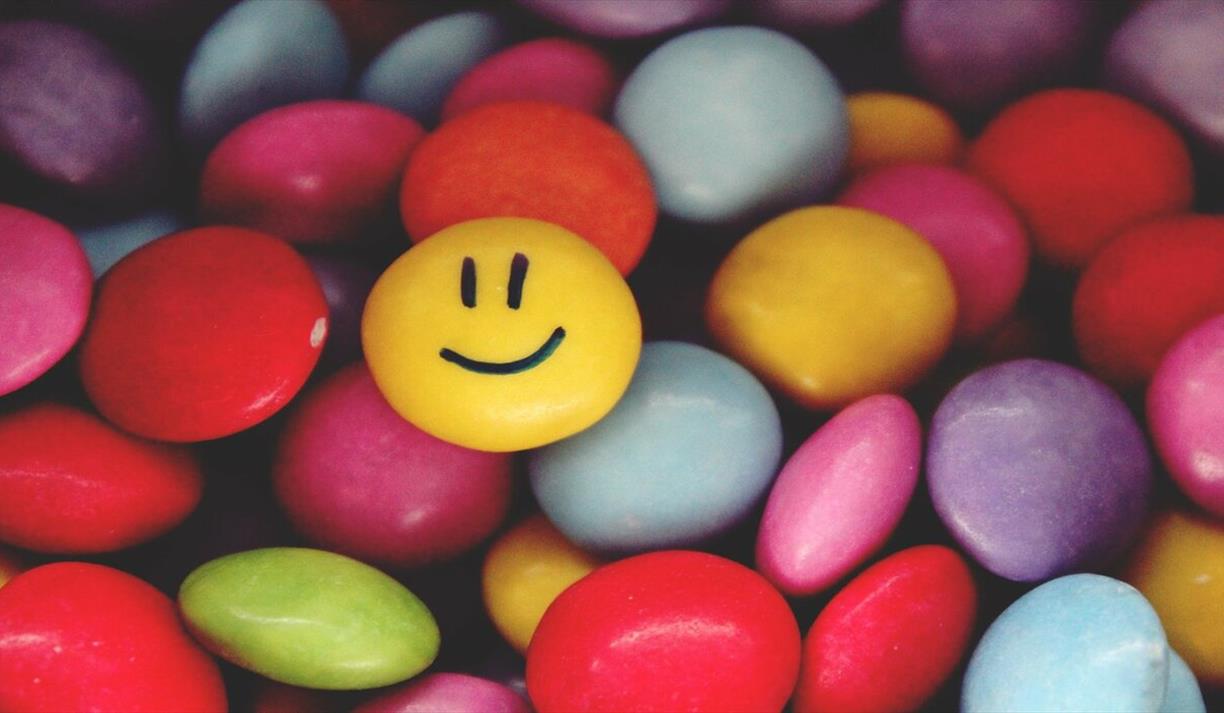 Multi-coloured candy with one yellow smiley faced candy on top