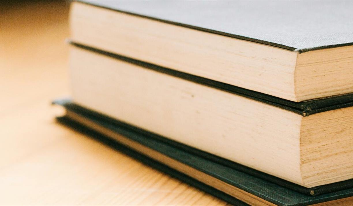 Close-up image of stack of hardcover books on a wooden table