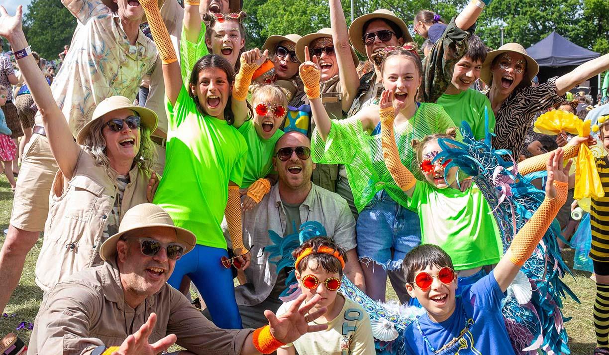 A group of people smile at the camera and raise their hands as they are excited to be at the Elderflower Fields festival.