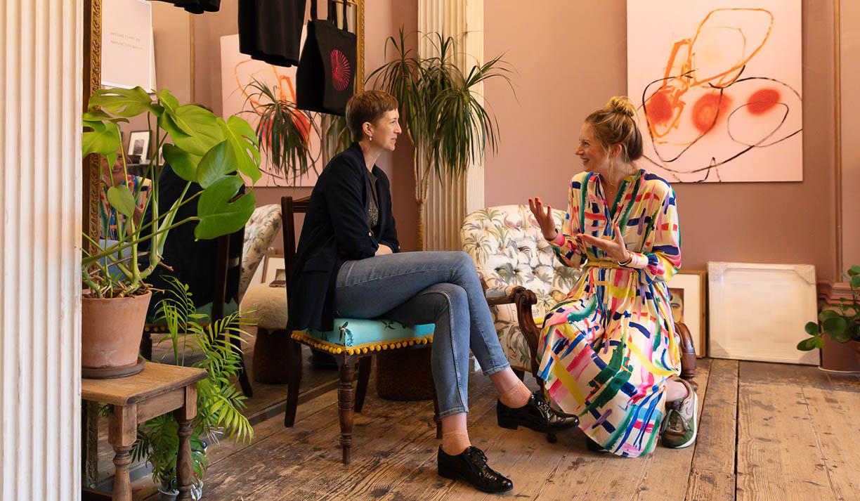 Two women sat on chairs animatedly discussing the artwork in the house. Photo credit: Syl Ojalla