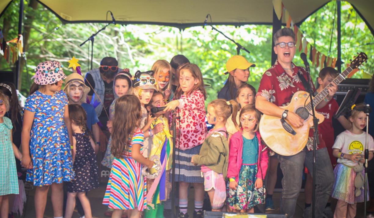 Children on a stage singing with Al Start who is playing the guitar.