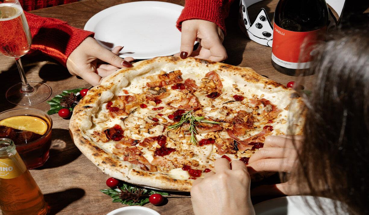 Diners at Franco Manca Brighton enjoying a tasty pizza. Image shows a close up of the pizza being shared by two people wearing red jumpers.