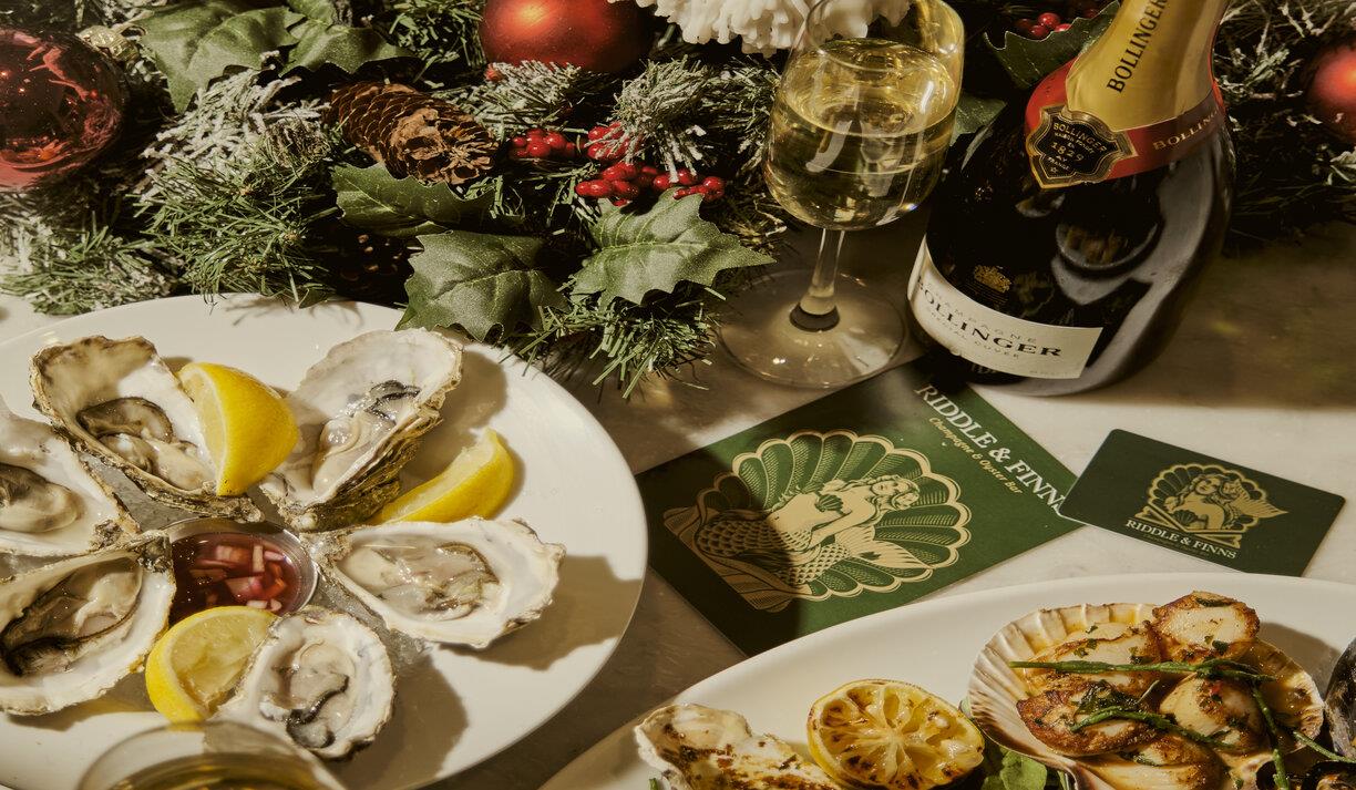 Image shows a platter of fresh seafood at Riddle & Finns in the Lanes. Oysters with lemon wedges next to a platter of scallops, with a bottle of Bolli