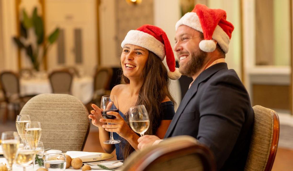 People in santa hats and drinking wine.