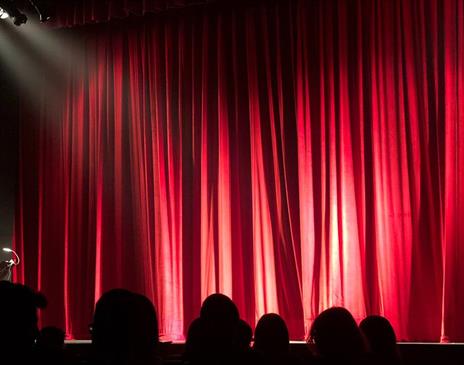 People sitting in a theatre in front of a red curtain