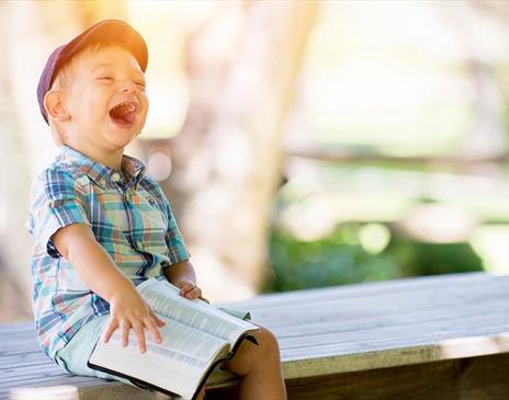 Boy sitting with book on a bench and laughing