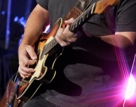 Man in black shirt playing a brown electric guitar