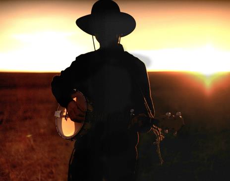 Silhouette of a person wearing a cowboy hat and playing a banjo