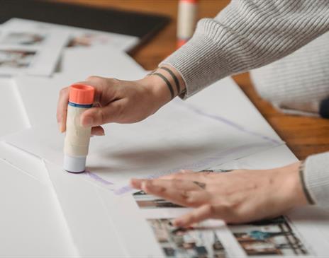 A person with tattoos using a glue stick on paper