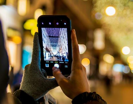 Person with one glove off taking a photo of a Christmas street light display