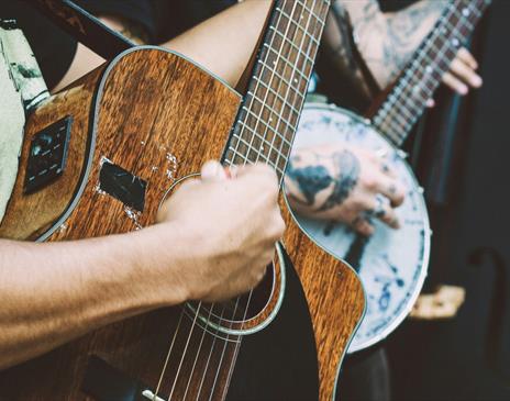 Person playing a banjo and another playing a dark wood acoustic guitar and another with a double bass