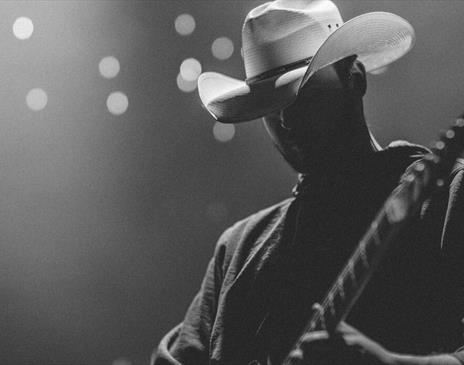 Person wearing a white cowboy hat playing on a lit stage