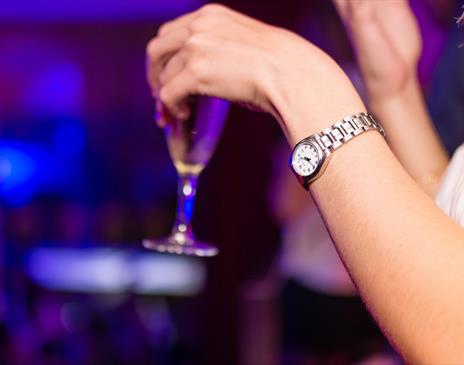 Hand with silver watch holding a glass