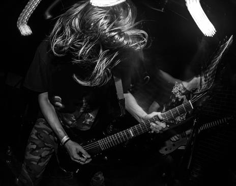 Black and white image of person with wild hair playing an electric guitar