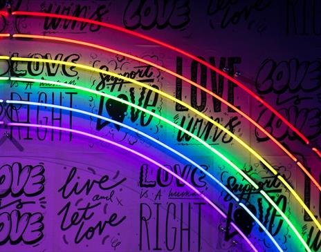 A neon rainbow sign with black writing behind it