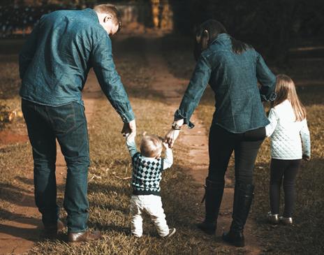 Young family walking a green forest and holding hands with their toddler