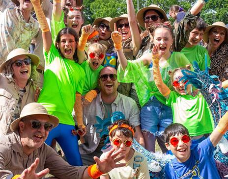 A group of people smile at the camera and raise their hands as they are excited to be at the Elderflower Fields festival.