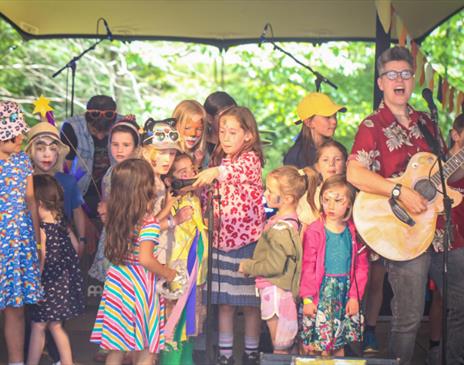 Children on a stage singing with Al Start who is playing the guitar.