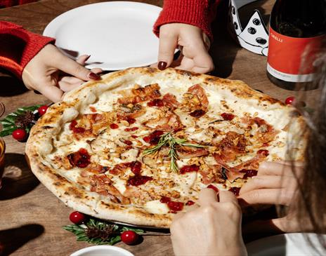 Diners at Franco Manca Brighton enjoying a tasty pizza. Image shows a close up of the pizza being shared by two people wearing red jumpers.
