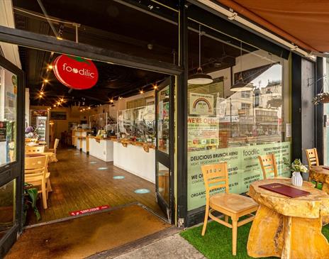 Outside of the restaurant, a Foodilic sign hangs in a doorway with real wooden furniture outside