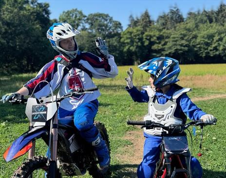 An adult and child on stationary motorbikes high fiving eachother.