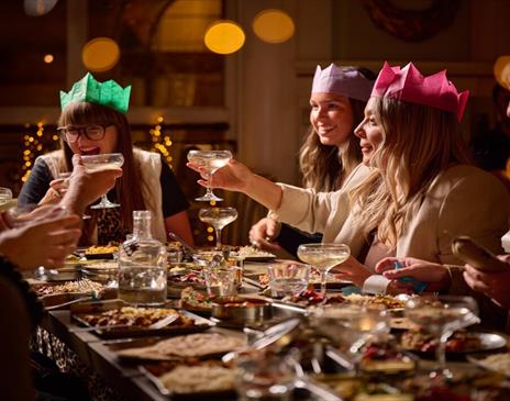 Partygoers enjoying a meal at Mowgli Brighton. a group of friends wearing colourful Christmas hats raise a toast, there are dishes of food in front of