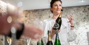 A tour of the estate, a woman holds a bottle of Wiston wine in her hand, and full glasses sit on the table.