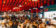 Inside Shelter Hall, Brighton. Diners enjoying food whilst colourful flags fly above them on the ceiling.
