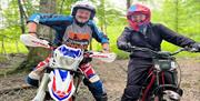 Two riders, with helmets, stationary and smiling at the camera.