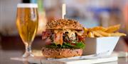 A burger and chips are sitting on the bar next to a glass of beer.