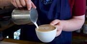 A barista pouring foam on a cup of coffee.