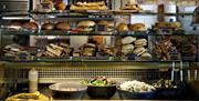 A glass counter laden with pastries, bowls of salad, sandwiches and bagels.