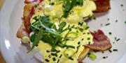 A white plate with eggs, bacon and hollandaise sauce.