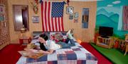 The Dolly Parton-themed room at Hotel Pelirocco. A woman is lying on a bed looking at Dolly Parton records. An American flag hangs behind her.