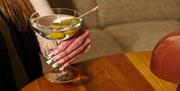 Image of a hand holding a martini cocktails with olives in it