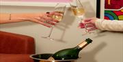 Two champagne flutes clinking with a bottle in the background