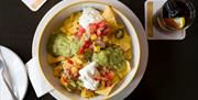 A bowl of delicious nachos with sour cream and jalapenos.