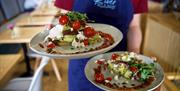 A person holding two plates of avocado toast with tomatoes on them.