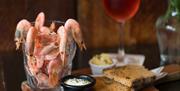 A pint of prawns and glass of wine sit next to a plate of bread.