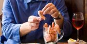 A guest digging into a pint of prawns with a glass of red wine and bread.